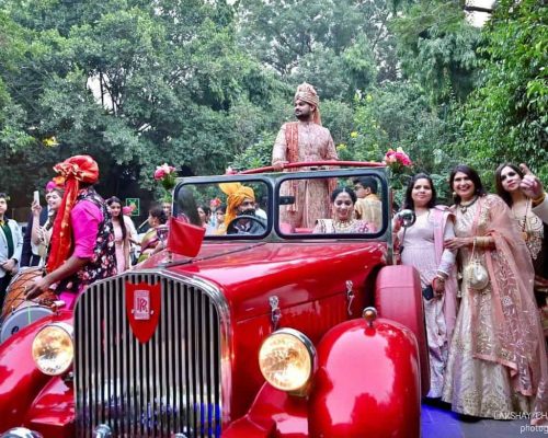 An indian groom feeling proud riding on a red vintage car