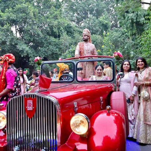 An indian groom feeling proud riding on a red vintage car
