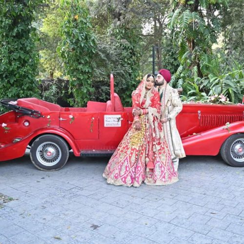 sikh couple having pre wedding shoot with red vintage car in a park with green background