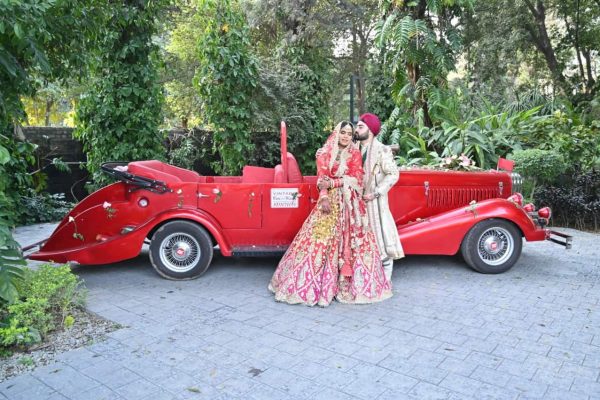 sikh couple having pre wedding shoot with red vintage car in a park with green background
